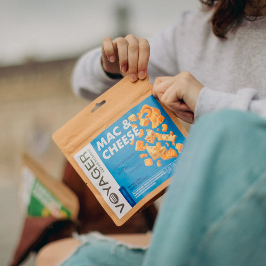 Istuva nainen avaamassa mac&cheese juustomakaroni retkiruokapussia