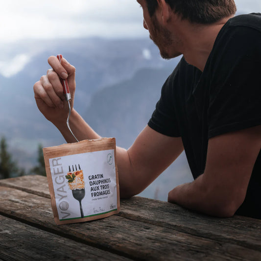 Mes istuu puupöydän ääressä ulkona ja syö retkiruokapussista kolmen juuston perunagratiinia.