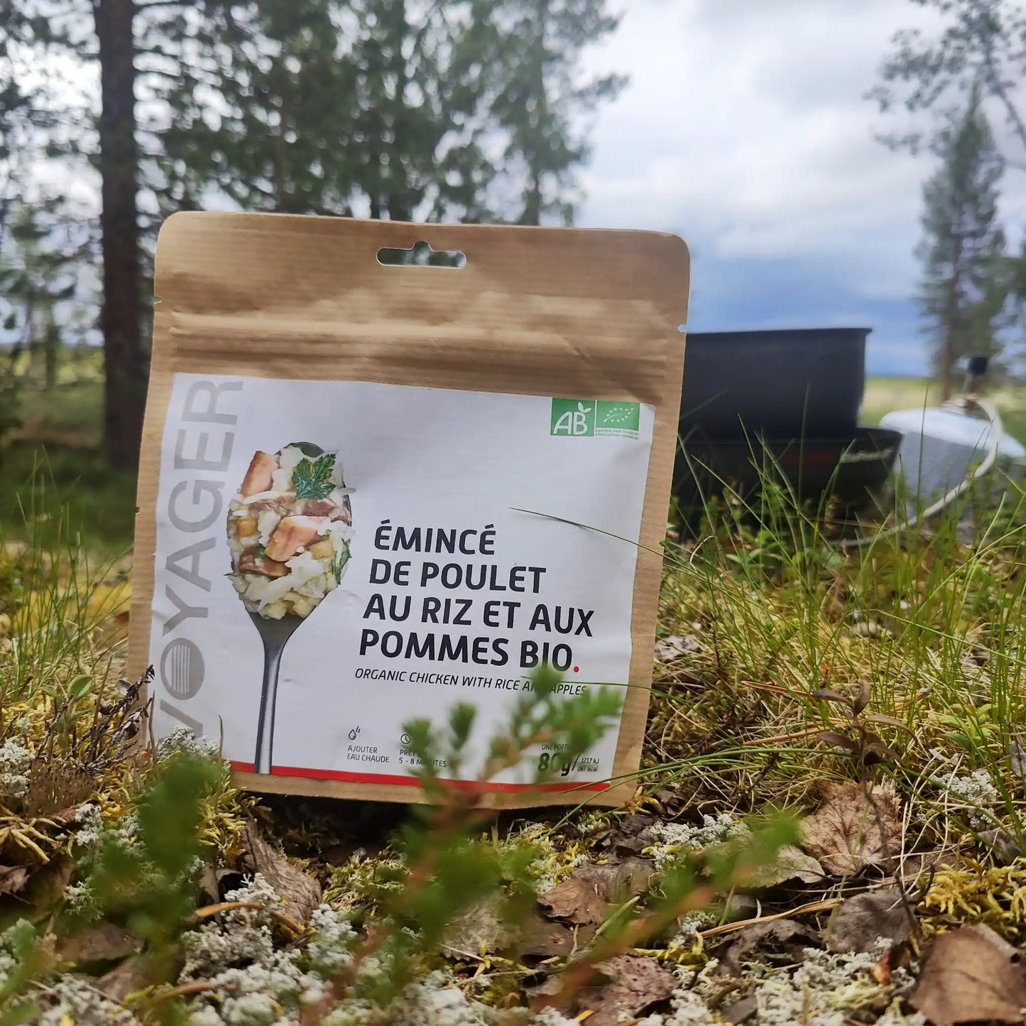 Omenaista kanaa ja riisiä ruohikkoisessa maassa, kaasukeitin ja puita taustalla.