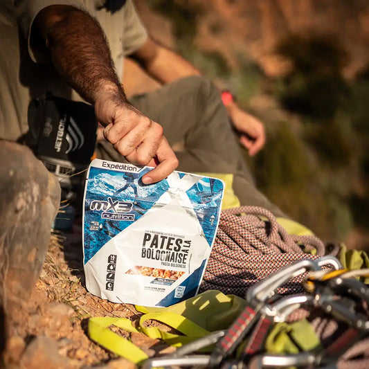 Mies ottamassa MX3 Pasta Bolognese retkiruokapussia maasta kiipeilyköysien vierestä.