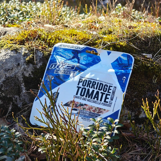 Retkiruoka juustoinen kaurapuuro tomaatilla maassa keväisessä varvikossa.