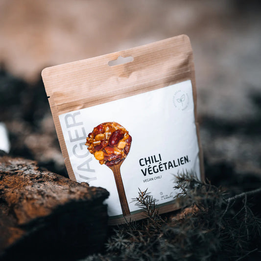 Chili sin carne vegaaninen retkiruoka kierrätettävässä pussissa maassa havujen vieressa.