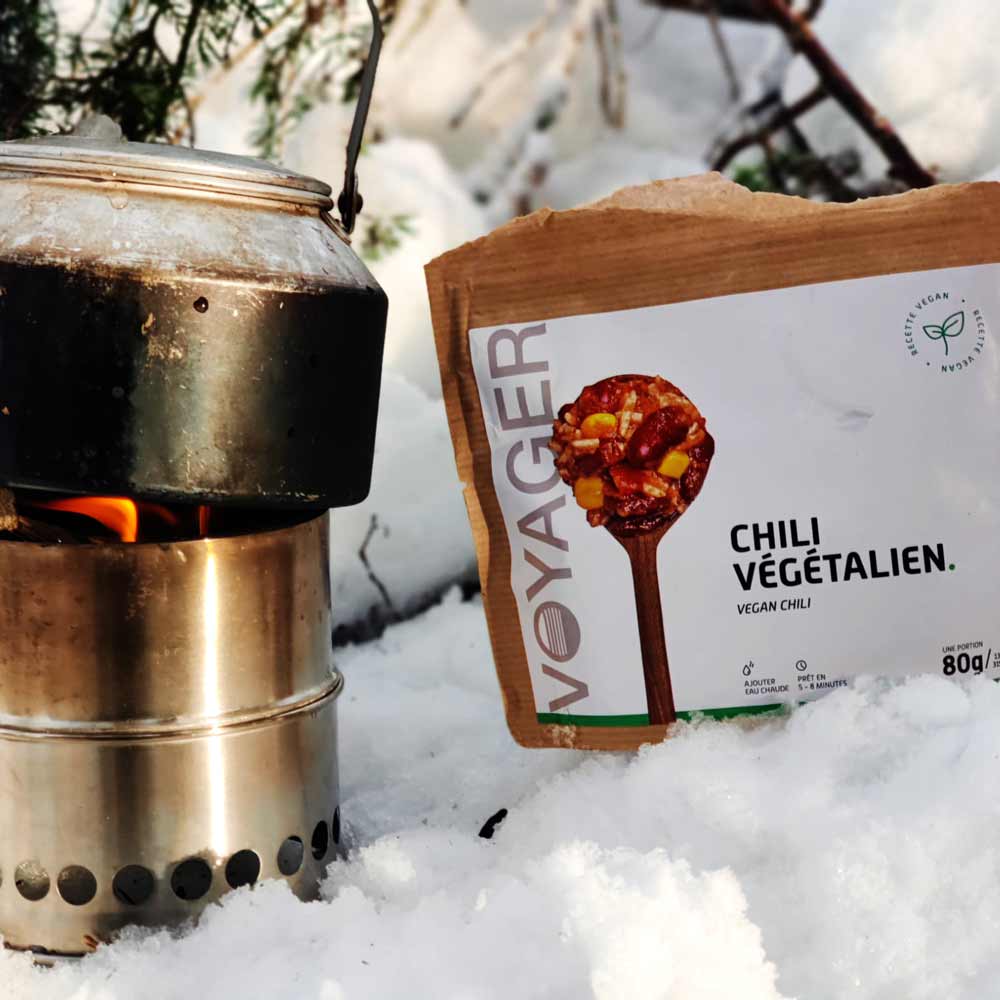 Chili sin carne retkiruokapussi lumihangessa risukeittimen ja vesipannun vieressä.