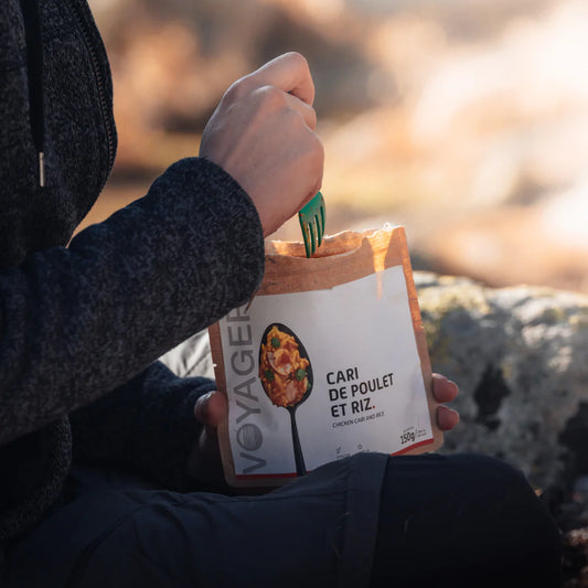 Kanacurry riisillä retkiruoka kierrätettävässä pussissa istuvan ihmisen sylissä, kädessä vihreä haarukka.