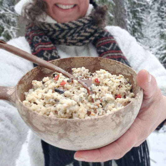 Kermainen sienirisotto retkiruoka kupilkalautasella valkotakkisen naisen kädessä.