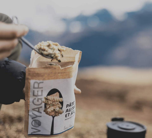 Lohipastaa ja tillilä retkiruokapussi avattuna ja ruokaa lusikassa, taustalla kattila ja vuoria.