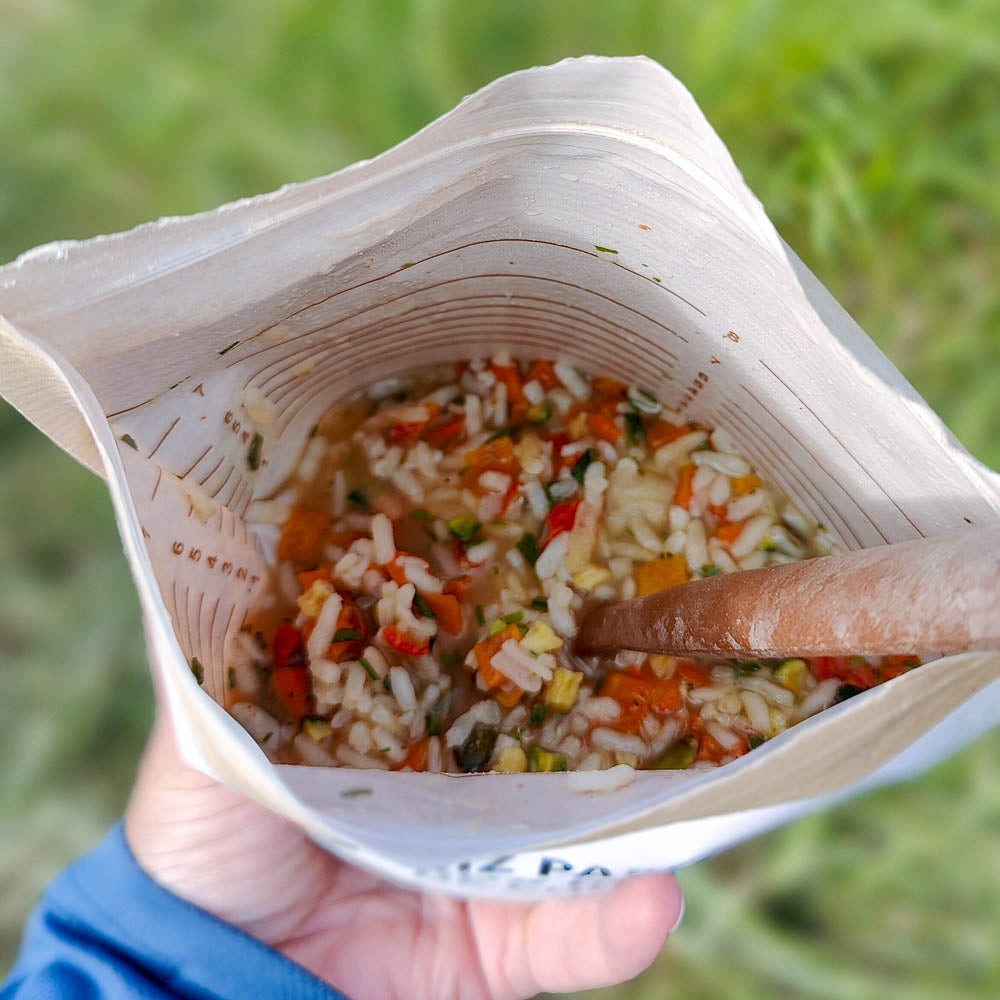 Mausteinen kasvisrisotto kurpitsansiemenillä retkiruokapussissa valmiina kädessä.