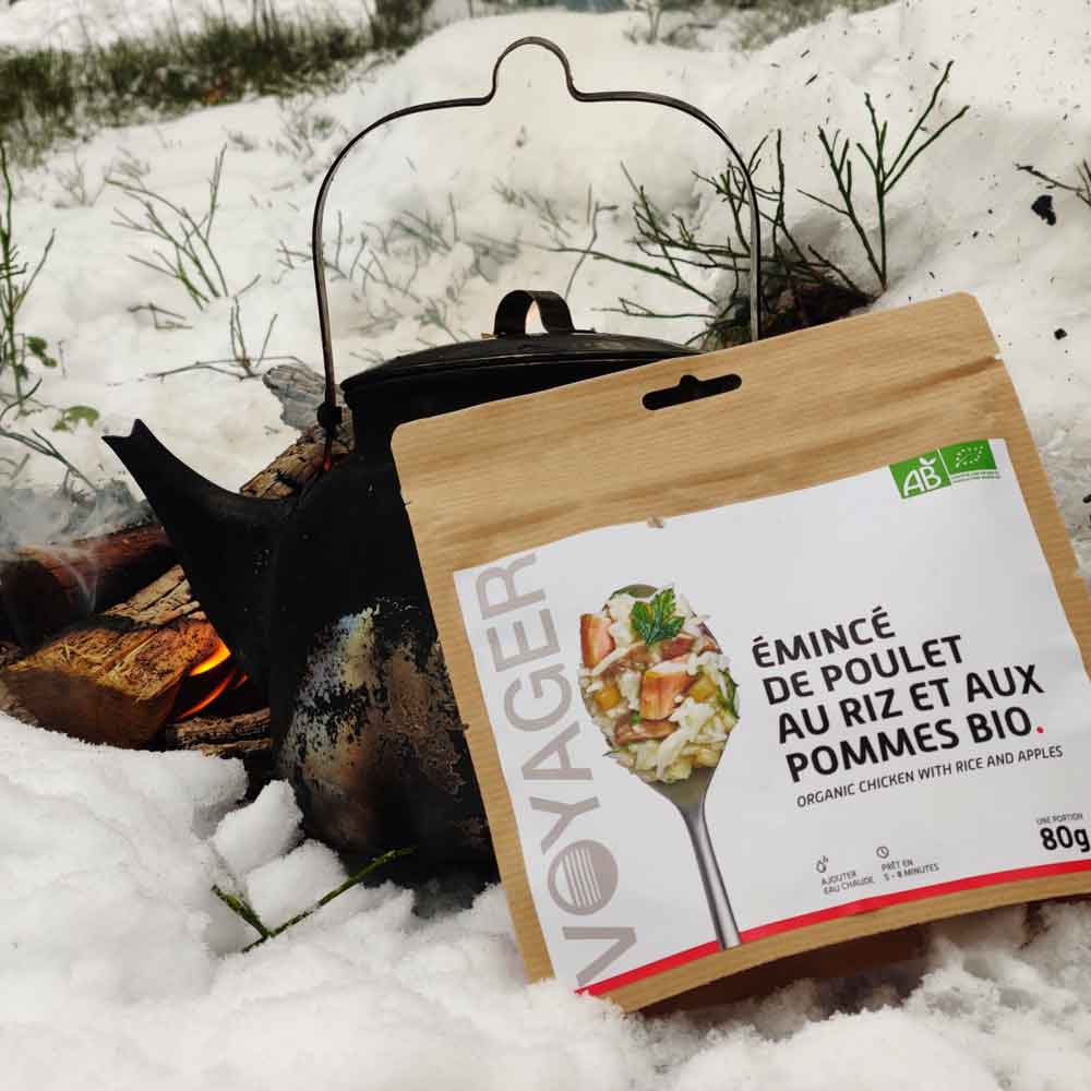 Omenaista kanaa ja riisiä-retkiruokapussi nokipannun ja nuotion edessä lumisessa maassa.