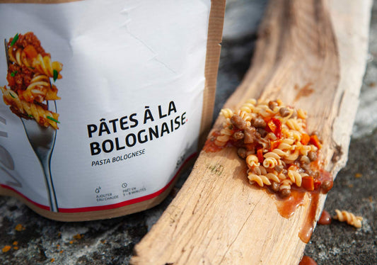 Pasta bolognese-retkiruoka pussi ja valmista retkiruokaa puun päällä.