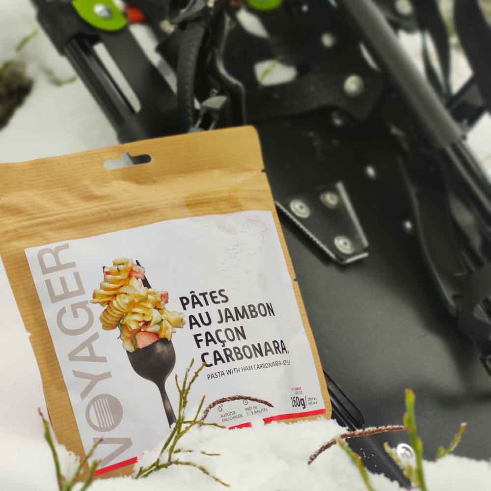 Pasta carbonara-retkiruokapussi lumisessa maassa, takana lumikengät.