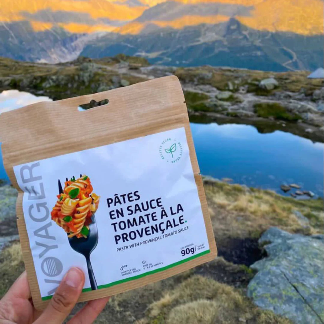Pasta provencal vegaaninen retkiruoka kierrätettävässä pussissa kädessä vuoristossa lammen ääressä.