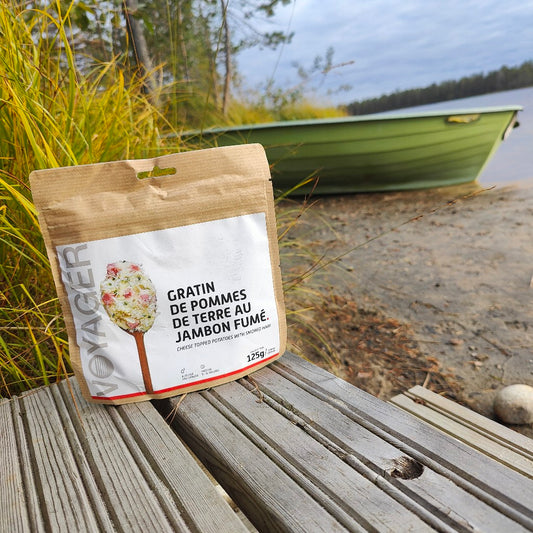 Perunagratiini savukinkulla retkiruokapussi laiturilla, takak rantahiekalla vihreä soutuvene.