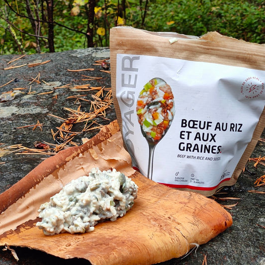 Härkäpata kurpitsansiemenillä retkiruokapussia kivellä edessä tuohi, jonka päällä valmista härkäpata-retkiruokaa.