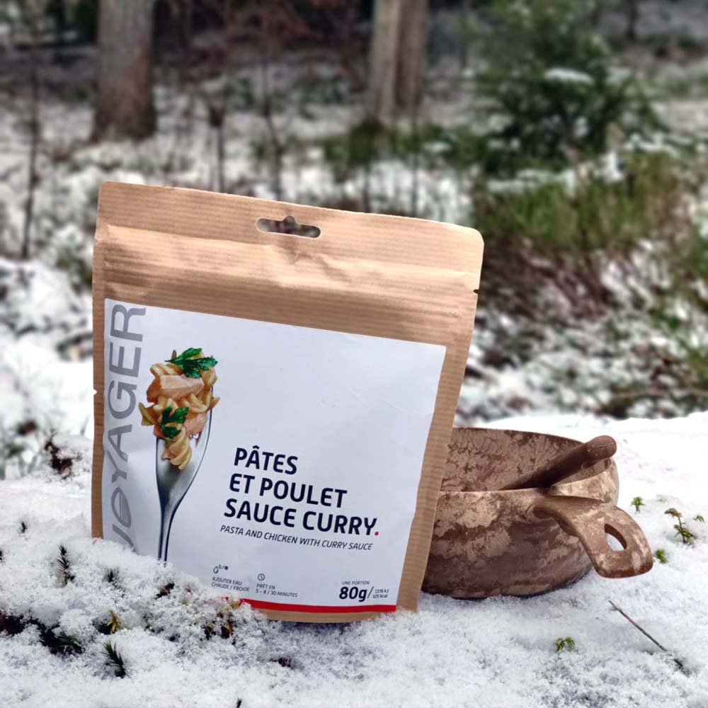 Kanaa ja pastaa currykastikkeessa retkiruokapussi ja kupilka-astia lumisessa maassa.