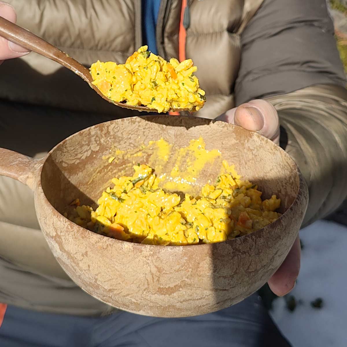 Kanacurry riisillä retkiruoka valmiina kupikassa ja lusikassa ihmisen kädessä.