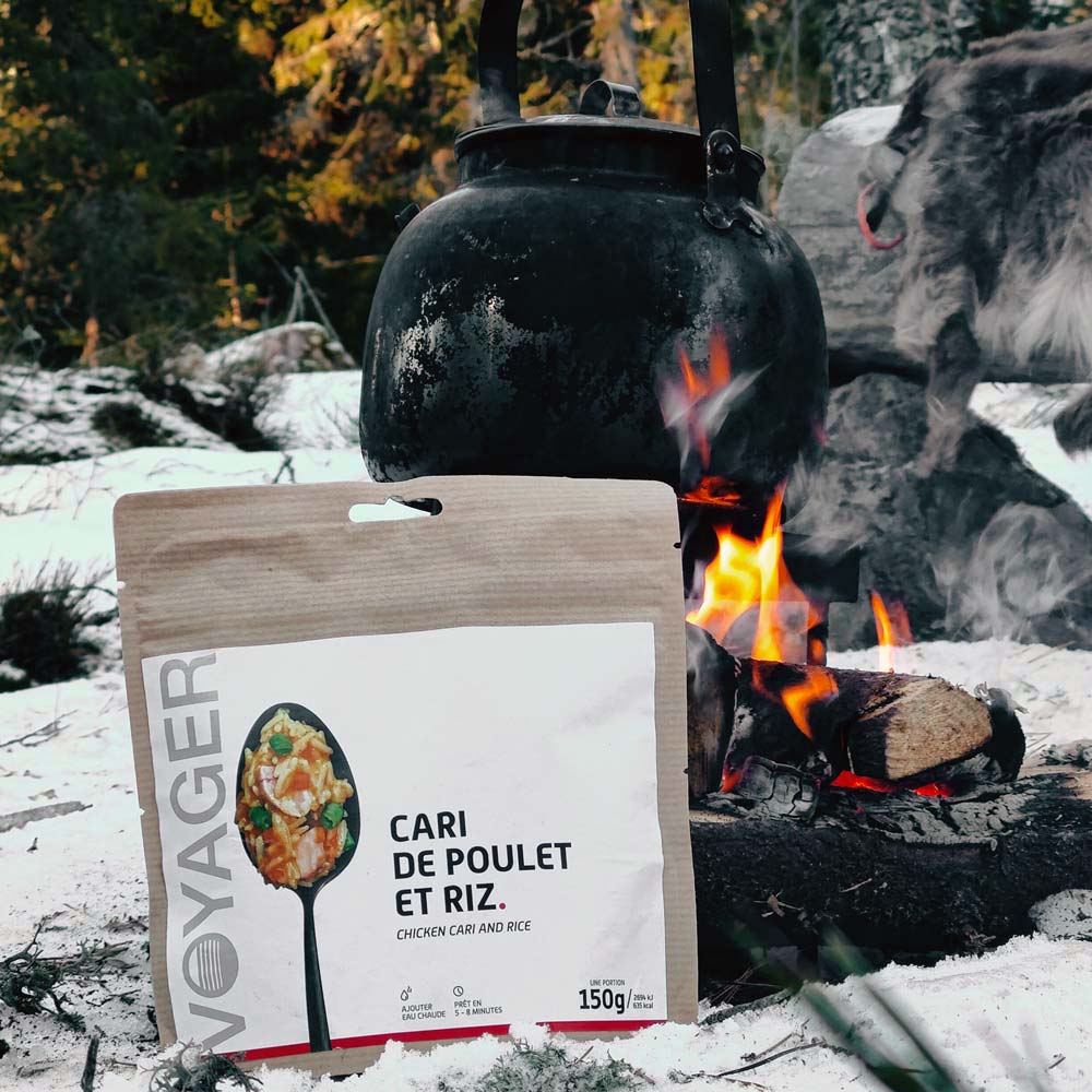 Kanacurry riisillä retkiruokapussi lumisessa maassa nuotion ja nokipannun edessä.
