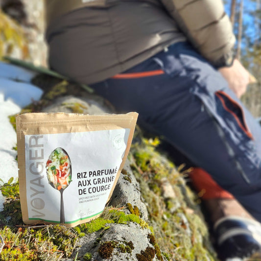 Mausteista kasvisrisottoa kurpitsansiemenillä, retkiruoka kierrätettävässä pussissa lumisella kalliolla takana istuu ihminen.