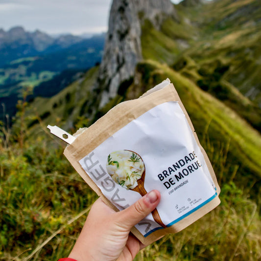 Turskapaistos retkiruoka pussi kädessä vehreässä vuoristossa, pussissa lusikka.