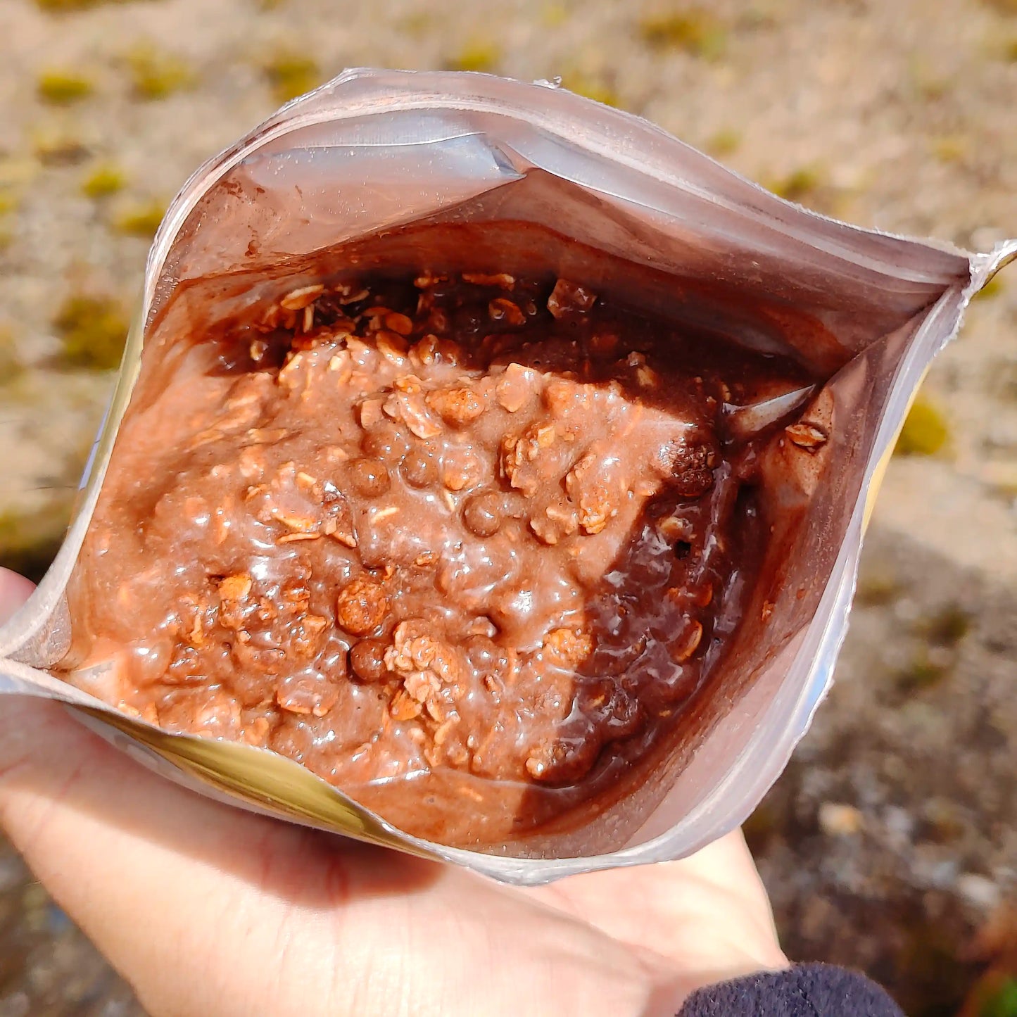 Suklaa-granolamysli retkiruoka valmiina kädessä avatussa pussissa..