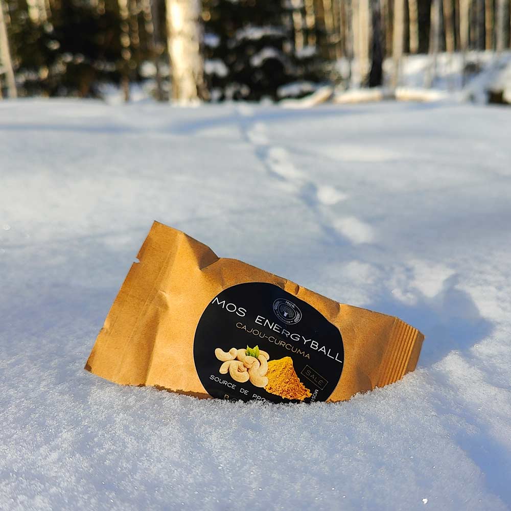 Retkiruoka välipala cashew-kurkuma energiapallo annospussi lumessa eläimen jälkien vieressä..