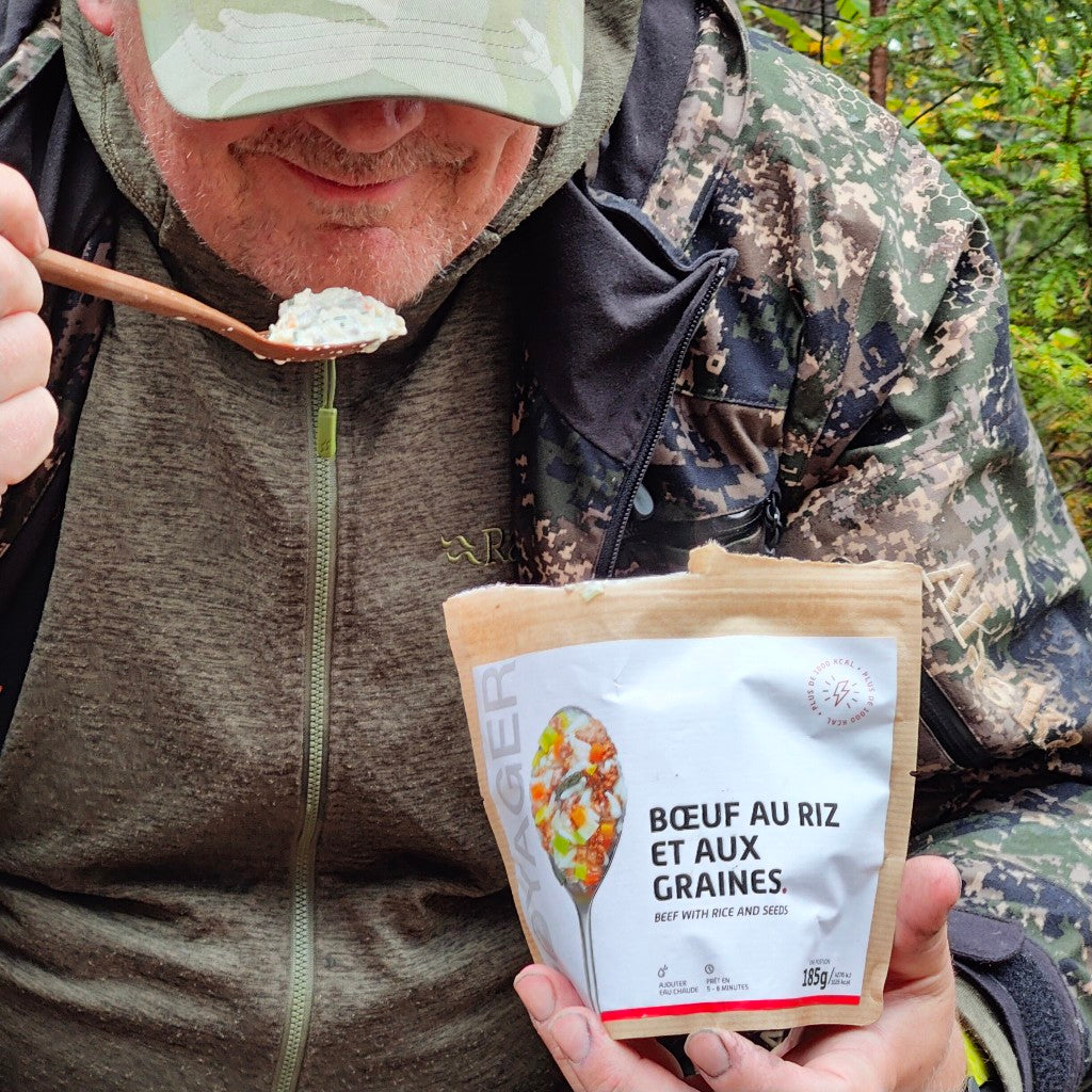 Istuva lippalakkipäinen maastopukuinen mies syö härkäpata kurpitsansiemenillä-retkiruokaa pussista.