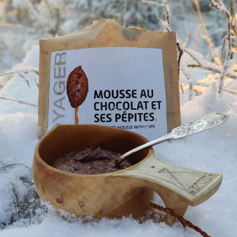 Suklaamousse suklaahipuilla-retkiruoka valmiina puisessa kuksassa lumisessa maassa, takana retkiruokapussi.