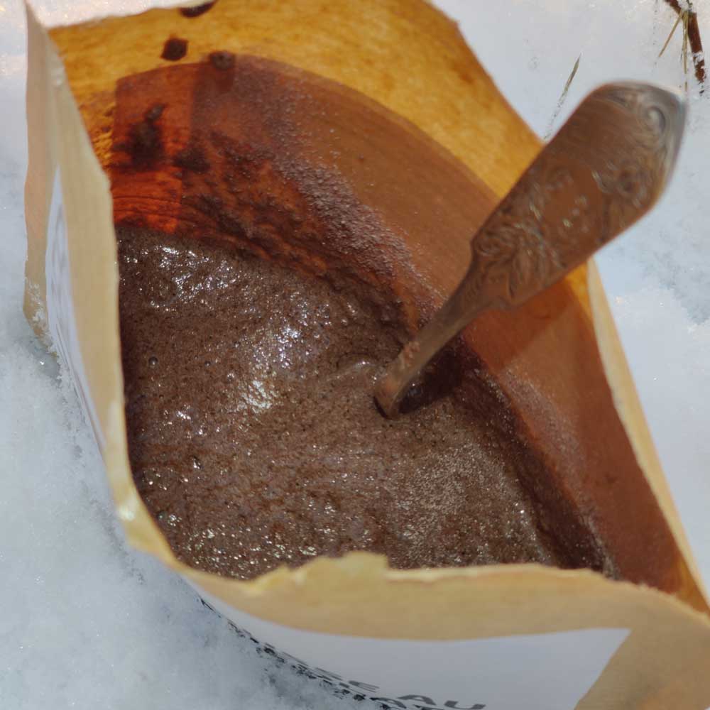 Suklaamousse suklaahipuilla-retkiruoka valmiina pussissa lusikan kera lumisessa maassa.